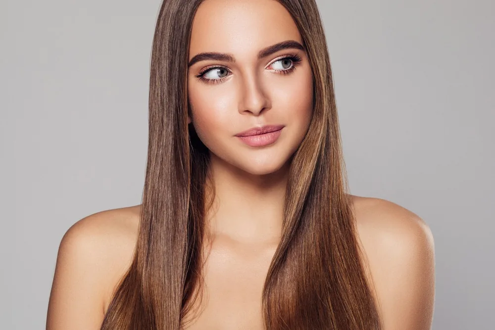 Woman with long, sleek straight brunette hair after a professional smoothing treatment in Warwick, RI